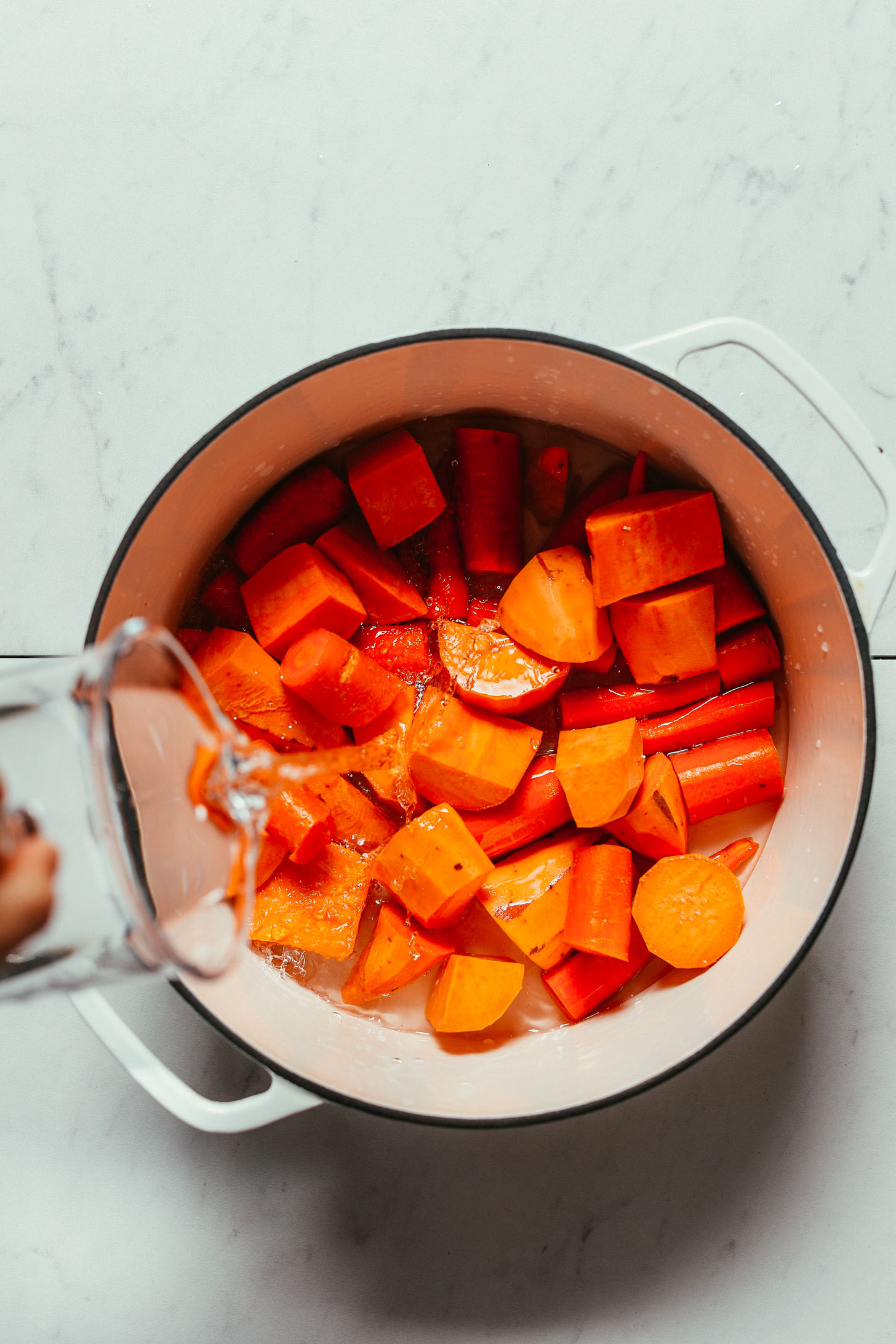 Pouring water over a pan of carrots and sweet potatoes for making our Mashed Sweet Potatoes recipe