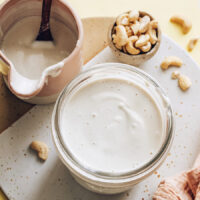 Jar and mini pitcher or cashew cream next to a bowl of raw cashews