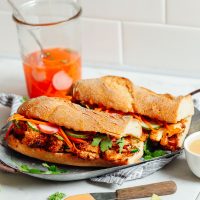 Two Cauliflower Banh Mi sandwiches on a plate with pickled veggies in a jar