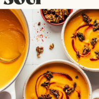Two bowls and a Dutch oven filled with our Creamy Carrot Ginger Soup recipe